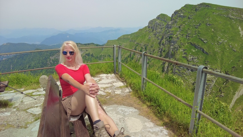 Tourist woman on a bench on top view of Monte Generoso or Calvagione Swiss mount. Aerial skyline of Lugano lake of Ticino canton. Top of cog train station in Mendrisio district, Switzerland.