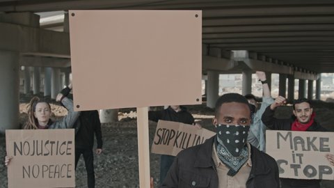 Portrait shot with slowmo of group of people with signs standing under highway bridge and protesting before camera