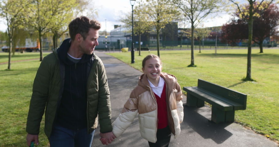 A front-view tracking shot of a caucasian father and daughter walking home from school together, they're holding hands and smiling. Royalty-Free Stock Footage #1075486793
