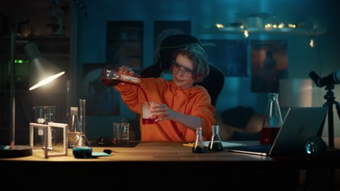 Smart Young Boy in Safety Goggles Mixes Chemicals in Beakers and Write Down Results on a Laptop. Teenager Conducting Educational Science Hobby Experiments, Doing Biology Homework in His Room.