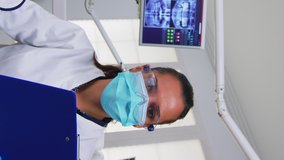 Vertical video: Dentistry doctor interrogating patient and taking notes on clipboard before surgery. Doctor and nurse working in modern orthodontic office, writing and examining person wearing