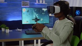 Black woman videogame player with vr goggles raising hands holding joystick after winning space shooter competition. Professional pro cyber playing online game with new graphics on powerful computer