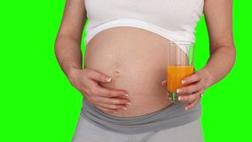 Pregnant woman stroking her belly and she is holding a glass of orange juice against a green screen