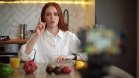 Close-up of female vlogger shooting culinary show speaking about exotic fruits looking at camera. Redhead young woman blogger recording live tutorial video about healthy vegetarian eating.