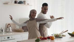 Happy Muslim Couple Dancing Having Fun Cooking Together In Modern Kitchen At Home. Family Of Two Laugh And Dance Enjoying Weekend And Dinner Preparation. Tracking Shot, Slowmo