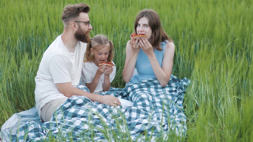 Young family having picnic eating  chocolate sandwiches. Woman feeding man. Happy family of three relaxing on green field
