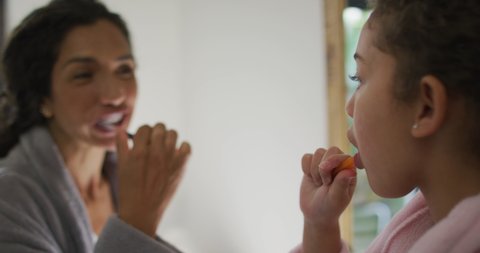 Happy mixed race mother and daughter brushing teeth in bathroom. domestic life and family leisure time concept.