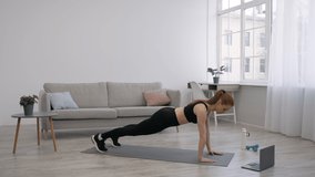 Sporty Woman Standing In Plank Doing Shoulder Touch Exercising At Laptop At Home. Online Gym Workout Concept. Female Having Fitness Training In Living Room. Side View