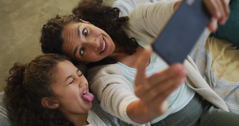 Happy mixed race mother and daughter laying on the floor,having fun and taking selfie. domestic life and family leisure time concept.