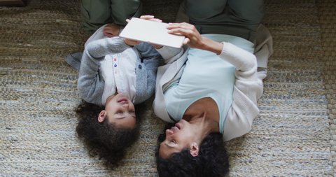 Happy mixed race mother and daughter laying on the floor,having fun and using tablet. domestic life and family leisure time concept.