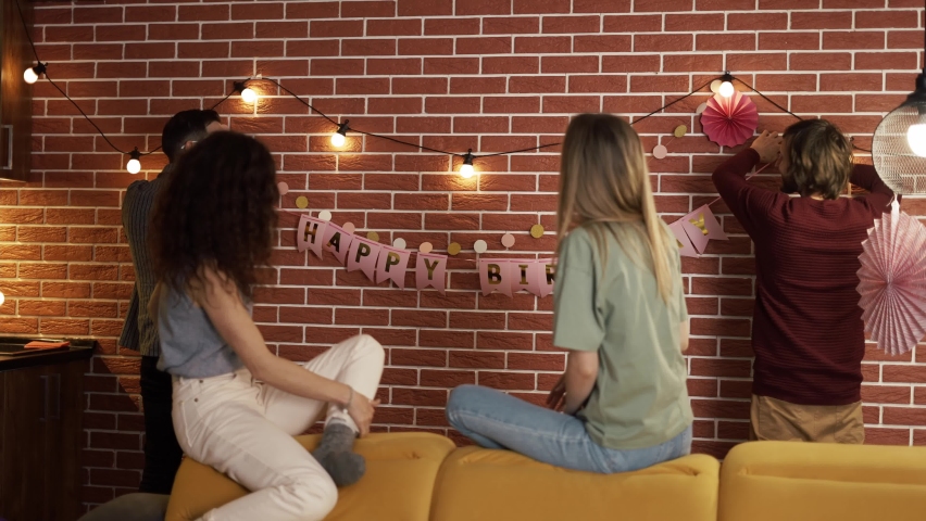Friends preparing party indoors, decorating living room