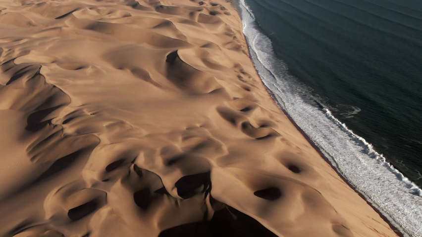 Aerial view of Sandwich Harbour, where towering sand dunes meet the Atlantic coast, near Walvis Bay in the Namib-Naukluft National Park, Namibia. Royalty-Free Stock Footage #1075507775