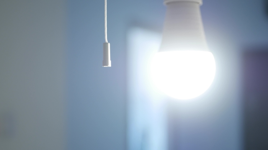 A Person Pulls the Switch Cord with His Hand and Turns Off the Light Bulb. Turning Off the Led Light in the Office Room. Royalty-Free Stock Footage #1075508381