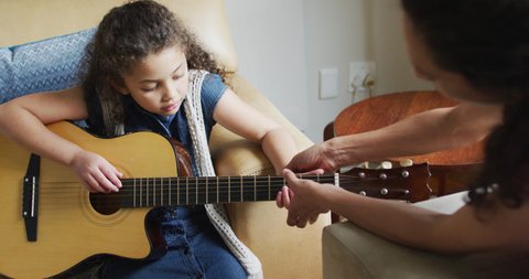 Happy mixed race mother and daughter playing with guitar. domestic life and family leisure time concept.