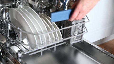 House chores concept.Housewife taking out clean plates from dishwasher machine. Female hands unloading dishwasher close up. Modern technologies for home