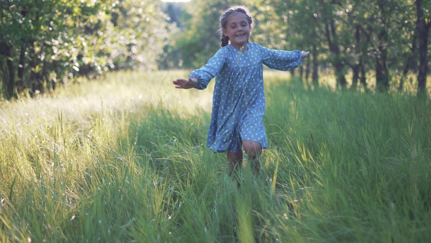 Happy girl. Little girl run through forest park. Kid plays on green grass. Happy kid run in garden. Green grass and trees in forest park. Little girl run through green garden.Happy girl among trees Royalty-Free Stock Footage #1075515968