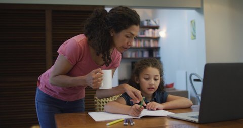 Happy mixed race mother and daughter doing homework together at home. domestic life and family leisure time concept.
