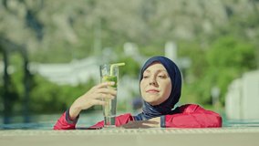 Young woman wearing hijab swimsuit swimming in the pool. A young woman wearing a hijab swimsuit cooling off in the pool enjoys her vacation by drinking lemon detox water. slow motion video 