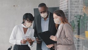 Caucasian business woman consultant insurance agent advises African American clients couple standing in office showing documents. Multiracial group partners wearing face medical masks discussing paper - Powered by Shutterstock - Get 15% off with code: PIKWIZARD15