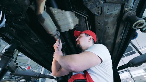 Auto mechanic tightens a part of car's underside with a wrench