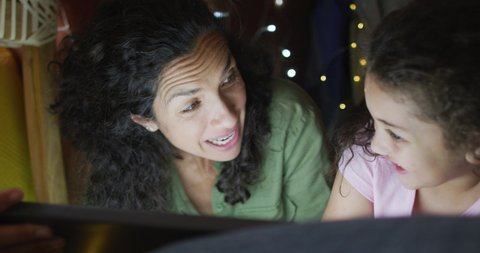 Mixed race mother and daughter using tablet in blanket tent. domestic life and family leisure time concept.