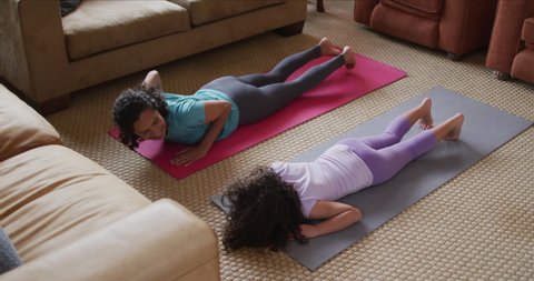 Mixed race mother and daughter practicing yoga in living room. domestic life and family leisure time concept.