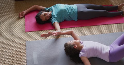 Mixed race mother and daughter practicing yoga in living room. domestic life and family leisure time concept.