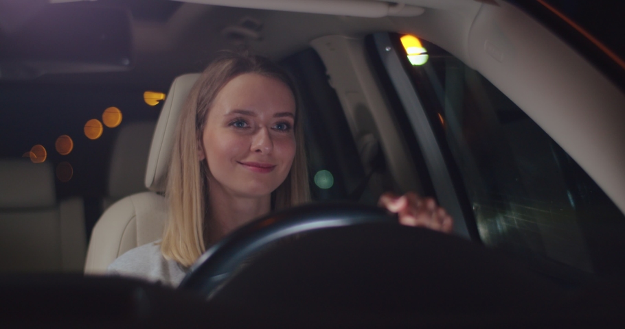 Freedom of the open road. Front view of joyful young woman relaxing on the front seat, driving their car and smiling with pleasure during the evening. People and transport concept Royalty-Free Stock Footage #1075521593