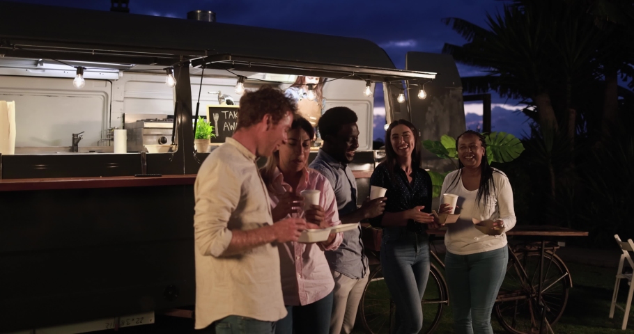 Multiracial people talking in front of food truck outdoor - Multigeneration friends having fun eating dinner outside at summer time 