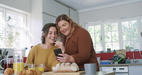Caucasian lesbian couple sitting at table using smartphone. domestic life, spending free time relaxing at home.