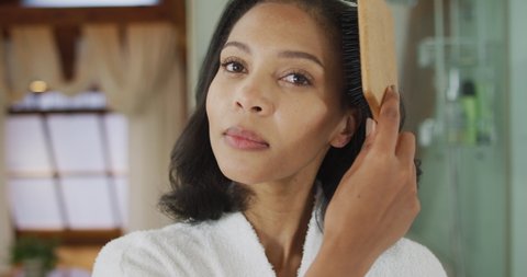 Portrait of mixed race woman wearing bathrobe brushing her hair. domestic life, spending quality free time relaxing at home.