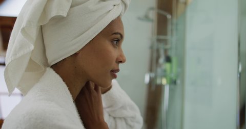 Mixed race woman wearing bathrobe looking at mirror. domestic life, spending quality free time relaxing at home.