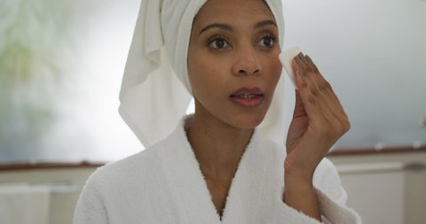 Mixed race woman wearing bathrobe cleaning her face. domestic life, spending quality free time relaxing at home.
