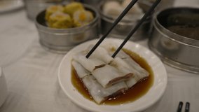 This POV video shows a pair of chopsticks grabbing a beef rice noodle from a dim sum dish.