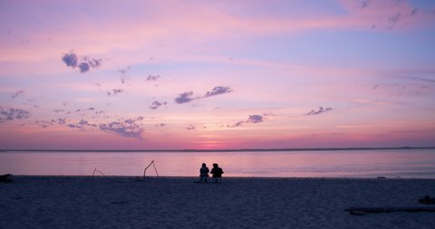 People sitting on chairs at sunset. Silhouettes from behind;