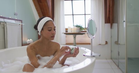 Mixed race woman taking a bath applying beauty face mask. domestic life, spending quality free time relaxing at home.