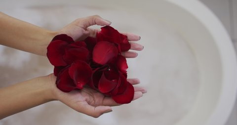 Mid section of mixed race woman taking a bath with rose petals. domestic life, spending quality free time relaxing at home.