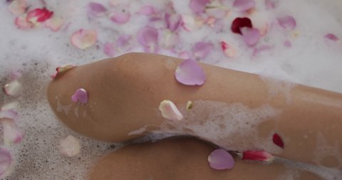Mid section of mixed race woman taking a bath with rose petals. domestic life, spending quality free time relaxing at home.