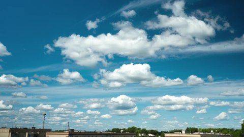 The movement of many small clouds over the rooftops. Video footage of a beautiful clear sunny blue sky with white fluffy clouds. The clouds move from left to right.