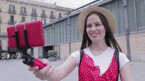 Smiling young woman tourist recording content for her travel vlog. Happy young female vlogger making video while waking talking about her holidays with mobile phone in the street - Millennial