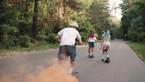 Group of four skaters ride through the park with a smoke bomb attached to the board. Crazy and dangerous action sport shot with professional skater.