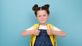 Cute smiling kid primary school girl with backpack showing thumbs up posing isolated on blue studio background. Happy caucasian child student celebrating freedom, recommending best education choice - Powered by Shutterstock - Get 15% off with code: PIKWIZARD15