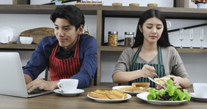 Asian couple wearing apron home cooking and dining while working with laptop
