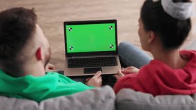 Back view of Caucasian young happy couple man and woman sitting at home and speaking online with green screen. Chroma key. Couple watching green screen in laptop. Shot behind models shoulders. - Powered by Shutterstock - Get 15% off with code: PIKWIZARD15