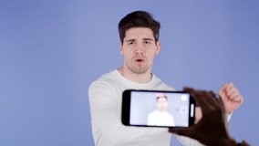 Smiling vlogger man recording video of hisself dancing in front of smartphone camera on purple background. Influencer makes funny social media clip