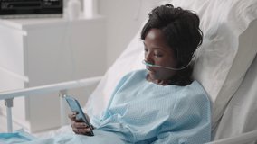 Black woman Patient in Hospital with Saline Solution Volumetric Infusion Pump using mobile phone on examination couch. African women lying in hospital bed with smart mobile phone while in hospital.