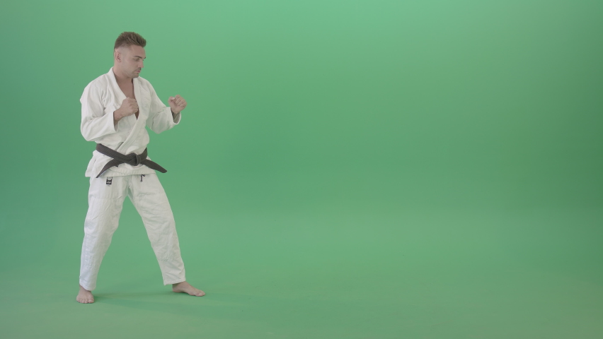 Jujitsu young man training slowly karate. Man in white karate clothes training moves and kicks isolated on green background. Martial arts taekwondo training footage. Royalty-Free Stock Footage #1075566410