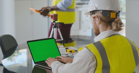 Over shoulder shot of civil construction engineer working with laptop at desk in office. Industrial engineer typing on computer in modern office. Green screen