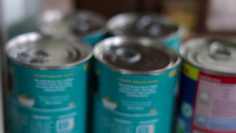 Cans Of Food Being Stored Up On Shelf By Man At Home
