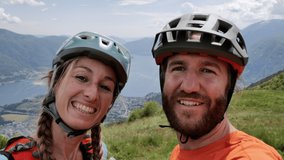 Happy couple taking selfie photo while enjoying mountain biking in summer. People doing sport activities in nature taking selfie